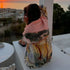 Person with a colorful scarf overlooking a sunset over a coastal town.